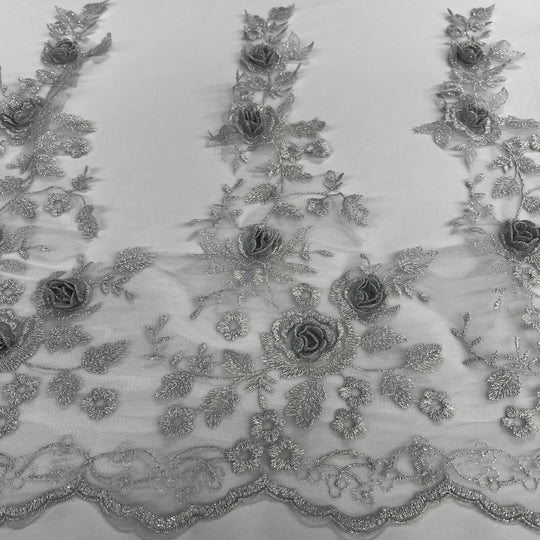 Silver floral embroidered lace trim featuring 3D rose appliqués, metallic thread embroidery, and a scalloped edge on soft tulle mesh., on a white background