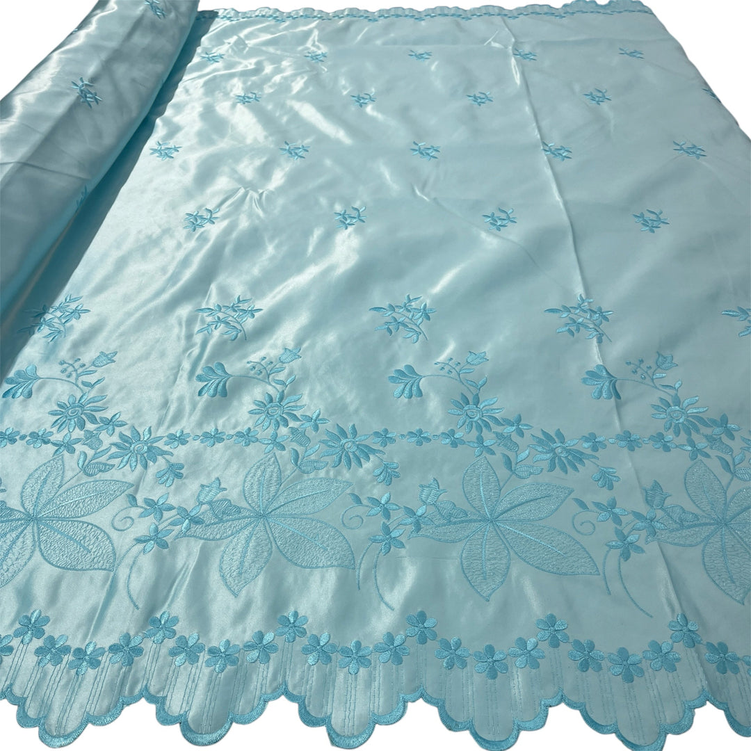 Aqua blue satin fabric with intricate light blue floral embroidery and a scalloped edge, shown partially rolled on the left against a white background.