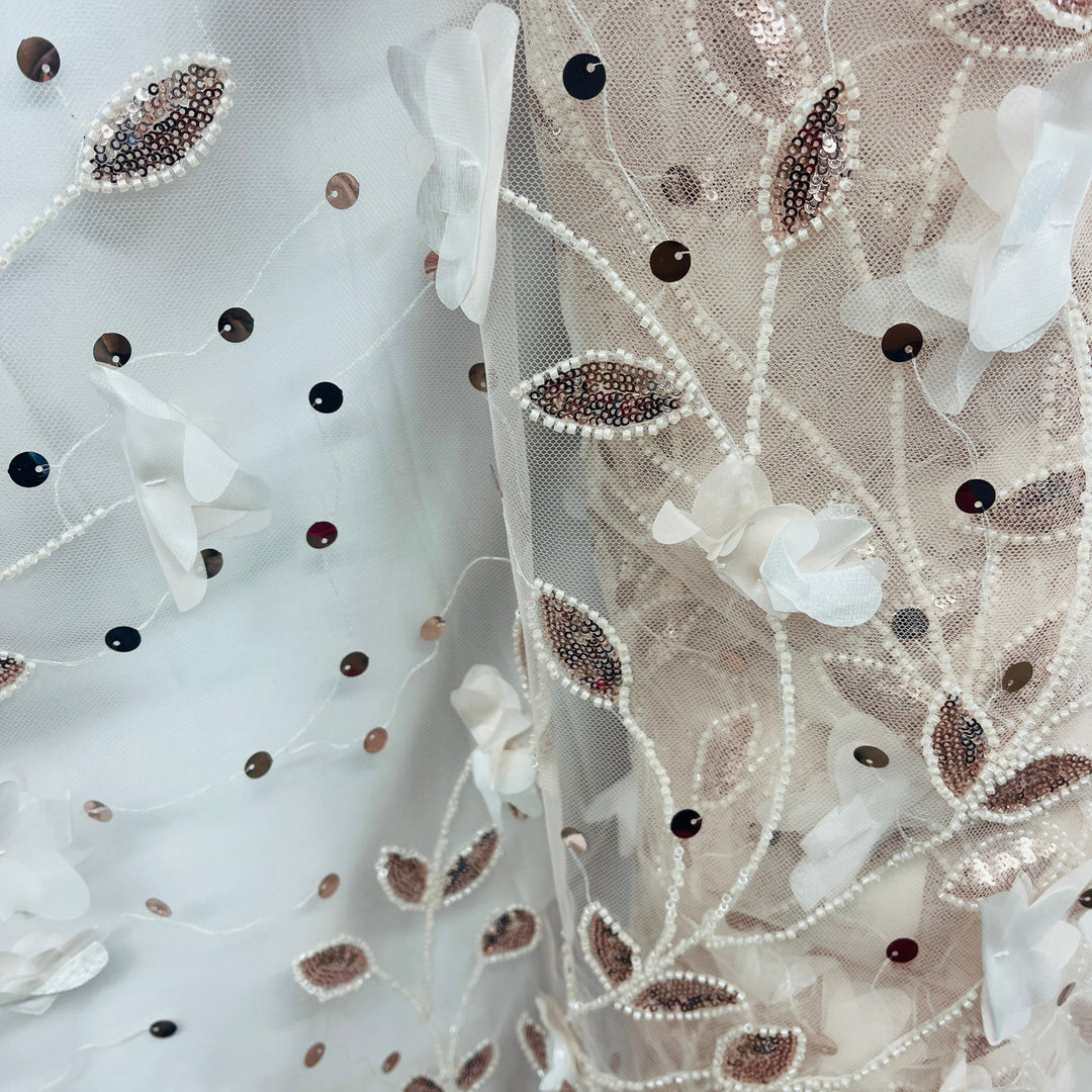Close-up of a decorative fabric featuring white 3D floral appliqués,  beaded and sequined  leaf and  pearl vine patterns on a sheer white mesh background.