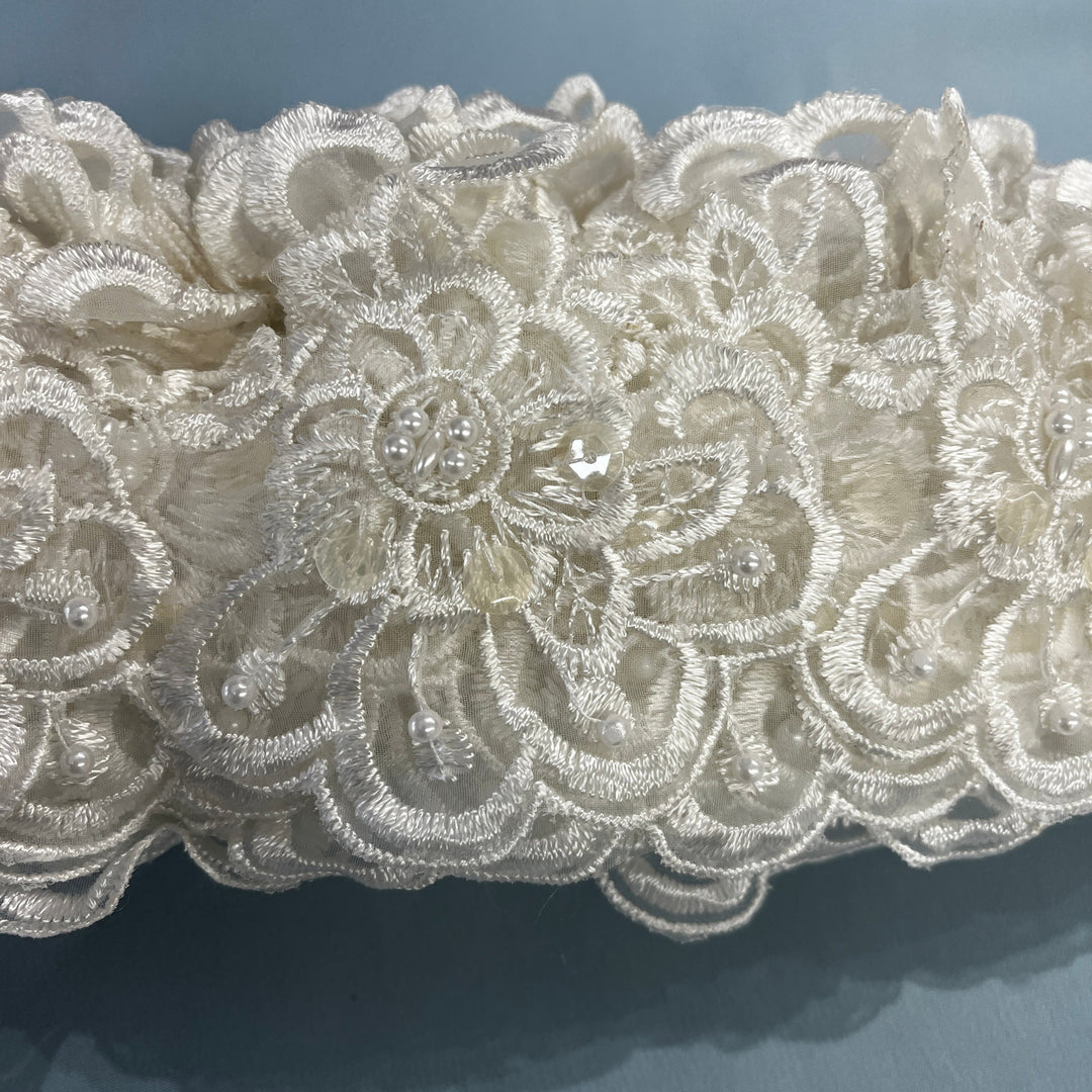 Close-up of an intricate ivory lace fabric with floral embroidery, bead details,  against a soft blue-gray background. LaceUSA #KZ-50