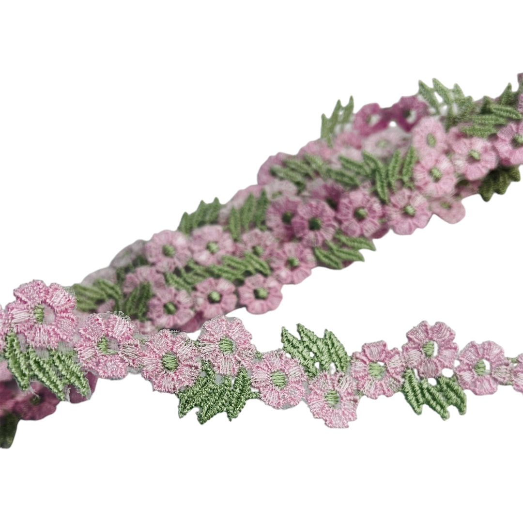 Closeup of Pink and  sage green floral lace trim with crocheted flowers and leaves, embroidered on organza on a white background.