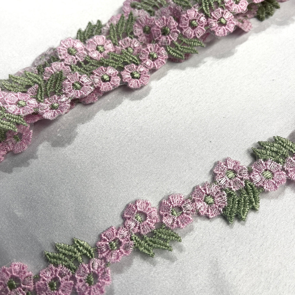 Closeup of Pink and green floral embroidered lace trim displayed diagonally on a light gray textured fabric background.Lace USA item 20441N Ping and sage