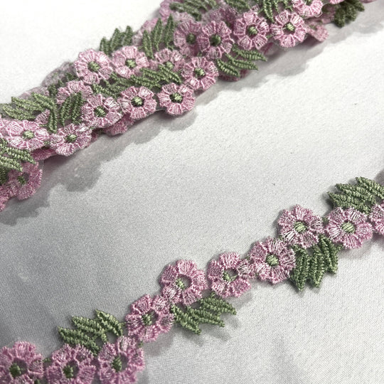 Closeup of Pink and green floral embroidered lace trim displayed diagonally on a light gray textured fabric background.Lace USA item 20441N Ping and sage