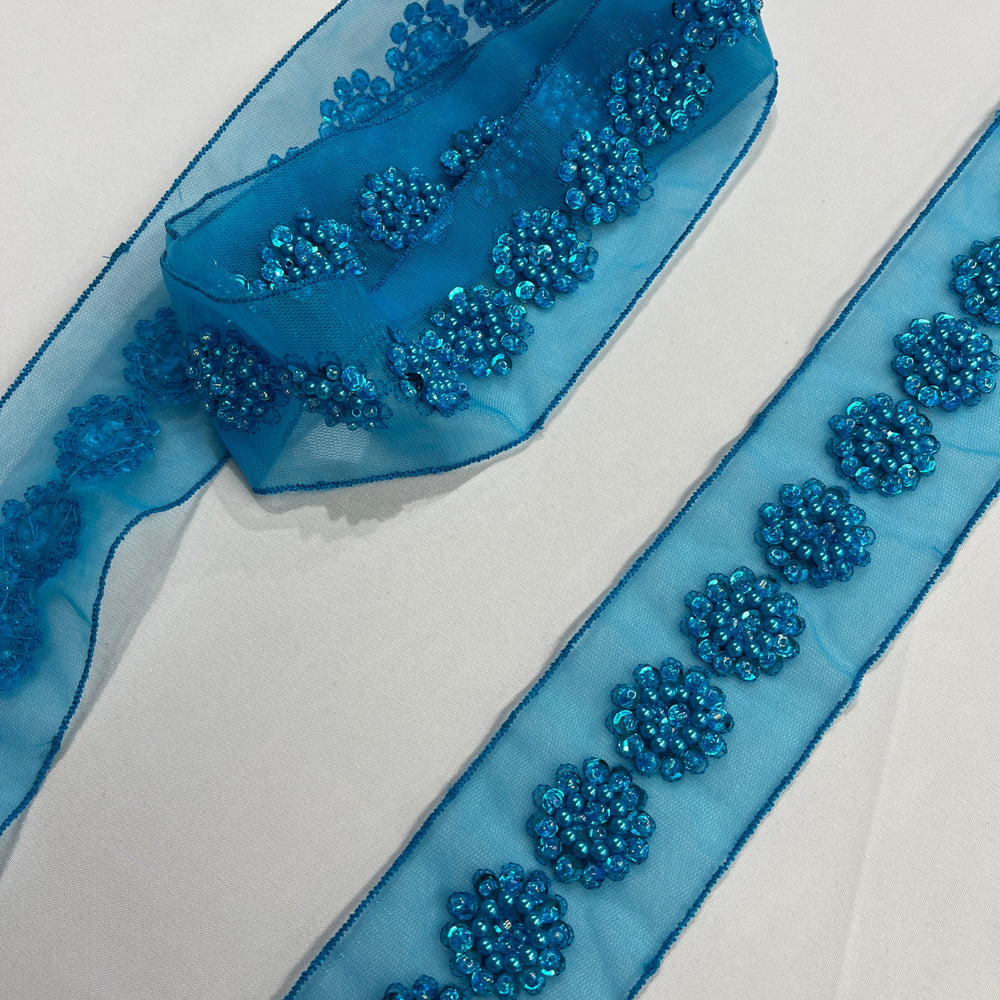 Turquoise sheer net mesh trim ribbon with beaded & sequined  floral patterns, laid diagonally, shown coiled and laid flat on a white background. Lace USA  #21766WNBP