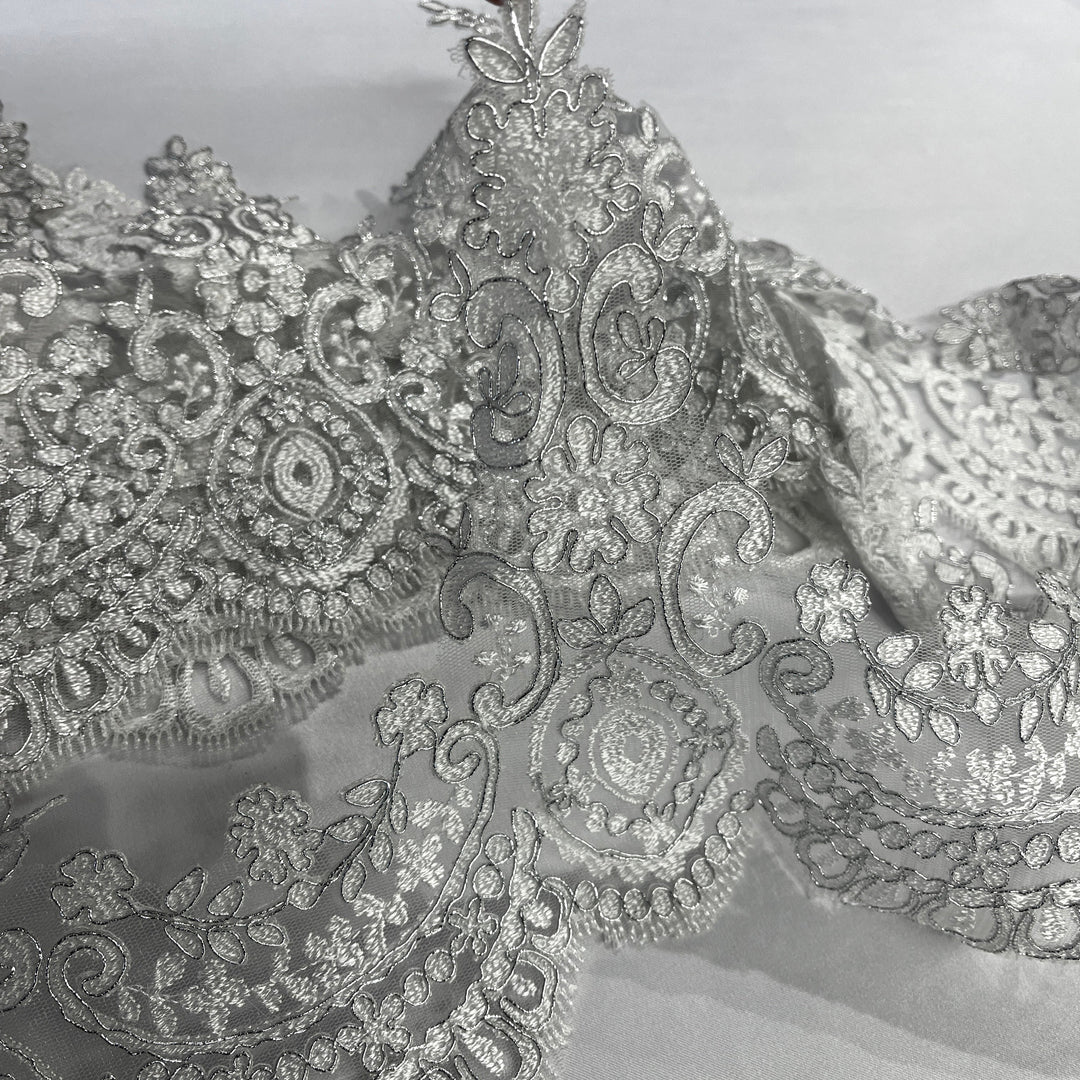 Closeup of White with silver cording floral lace trim with ornate embroidery and scalloped edging, displayed on a white background.  Lace USA 96794W  