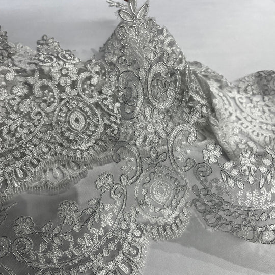Closeup of White with silver cording floral lace trim with ornate embroidery and scalloped edging, displayed on a white background.  Lace USA 96794W  
