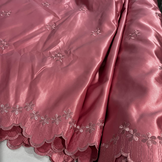 A close-up of a dusty rose  satin fabric with a scalloped edge and embroidered floral details.