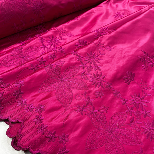 Fuchsia satin fabric with  embroidered floral motifs and a scalloped edge, shown in a close-up product shot.