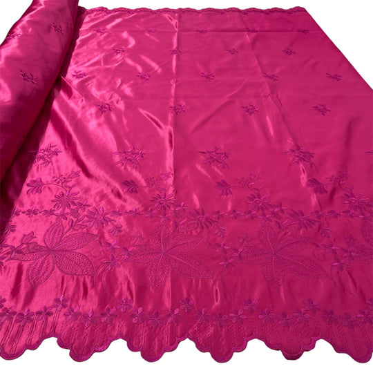 Fuchsia satin fabric with embroidered floral motifs and scalloped edge, partially rolled on white background.
