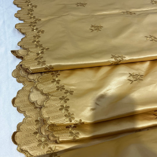 Gold satin fabric with embroidered floral motifs and a scalloped embroidered border, shown folded on a white background.