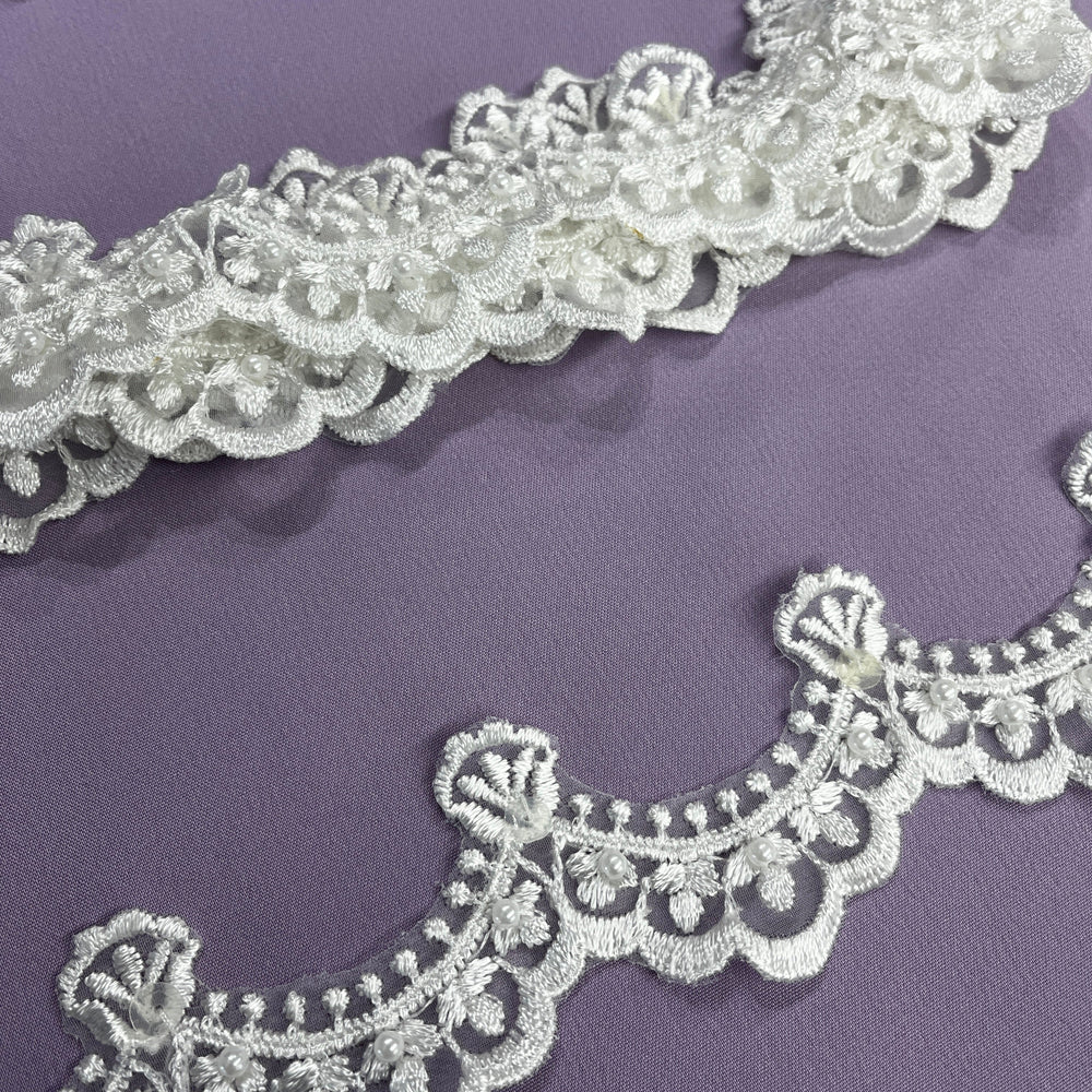 Off White Ivory embroidered lace trim on organza embellished with pearls and sequins with floral and scalloped patterns laid on a solid purple background. LaceUSA  Item 20648NBP 