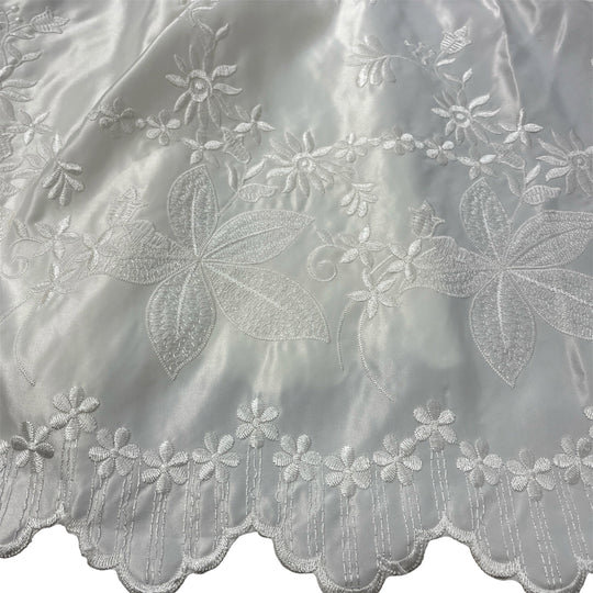 Ivory embroidered lace fabric with floral design, featuring a scalloped edge on a white background.