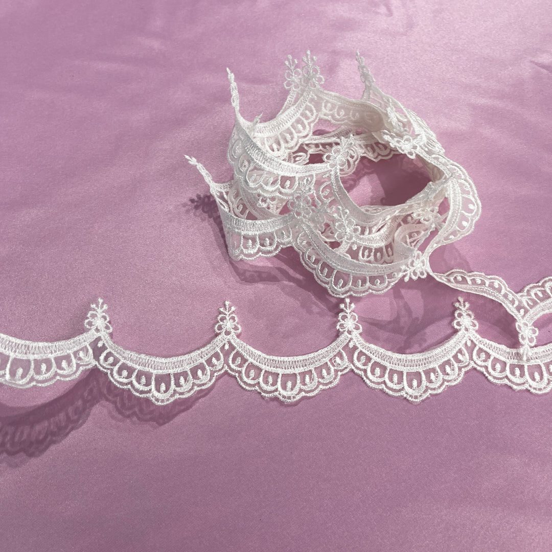 Ivory - Off White lace trim with an ornate scalloped edge, shown draped across a lavender background. LaceUSA  21618N