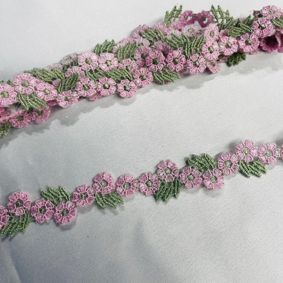 Pink and green floral embroidered lace trim displayed diagonally on a light gray fabric background.  Lace USA - 20441N
