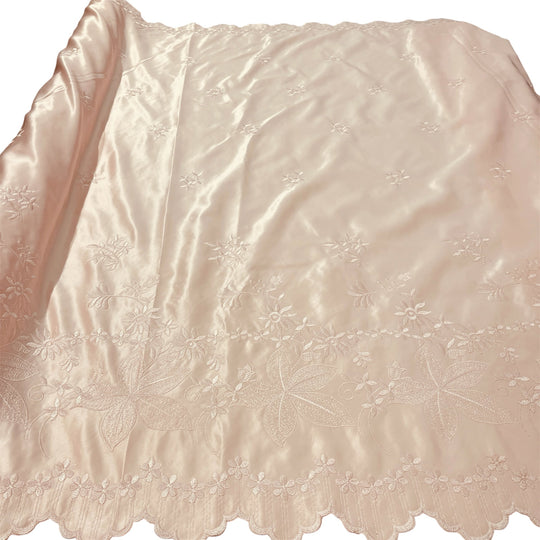 A light peach satin fabric with delicate floral embroidery and a scalloped embroidered border, shown laid flat against a white background.