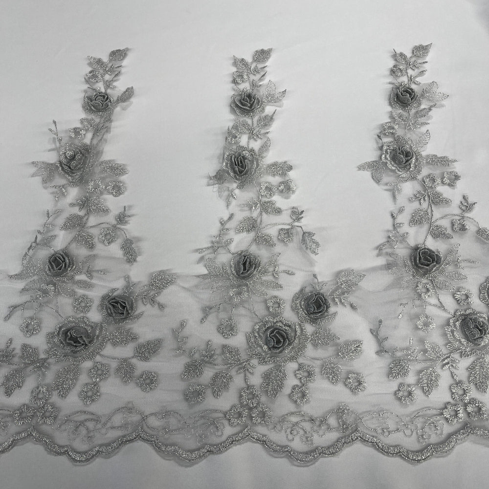 Silver floral embroidered lace trim featuring 3D rose appliqués, metallic thread embroidery, and a scalloped edge embroidered on net mesh., shown laid flat against a white background. LaceUSA #21854W