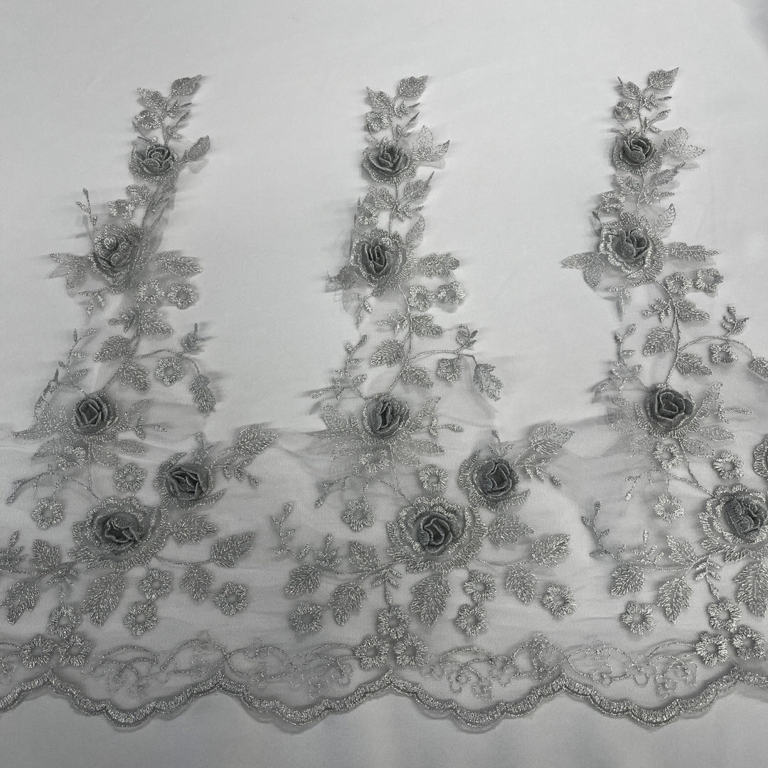 Silver floral embroidered lace trim featuring 3D rose appliqués, metallic thread embroidery, and a scalloped edge embroidered on net mesh., shown laid flat against a white background. LaceUSA #21854W