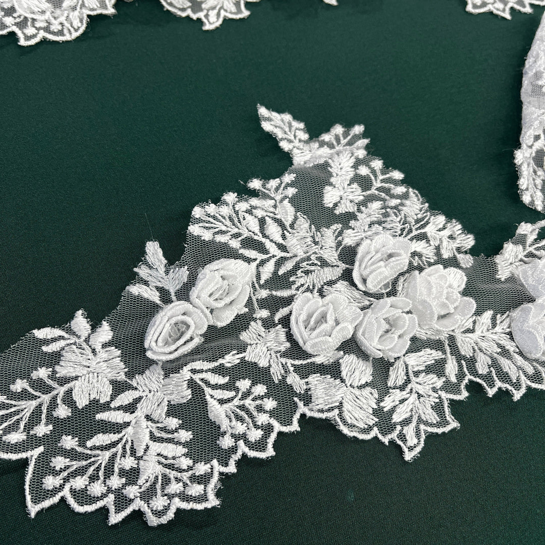 Closeup of White floral lace applique with embroidered  3D rose motifs and delicate leaf patterns, laid flat on a dark green background. Lace_USA #21853W