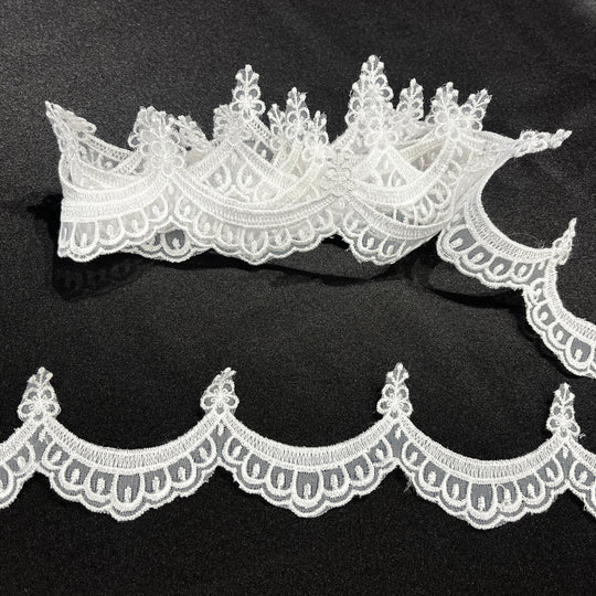 White lace trim with ornate floral and scalloped edges, embroidered on organza,  shown laid flat on a black  background.