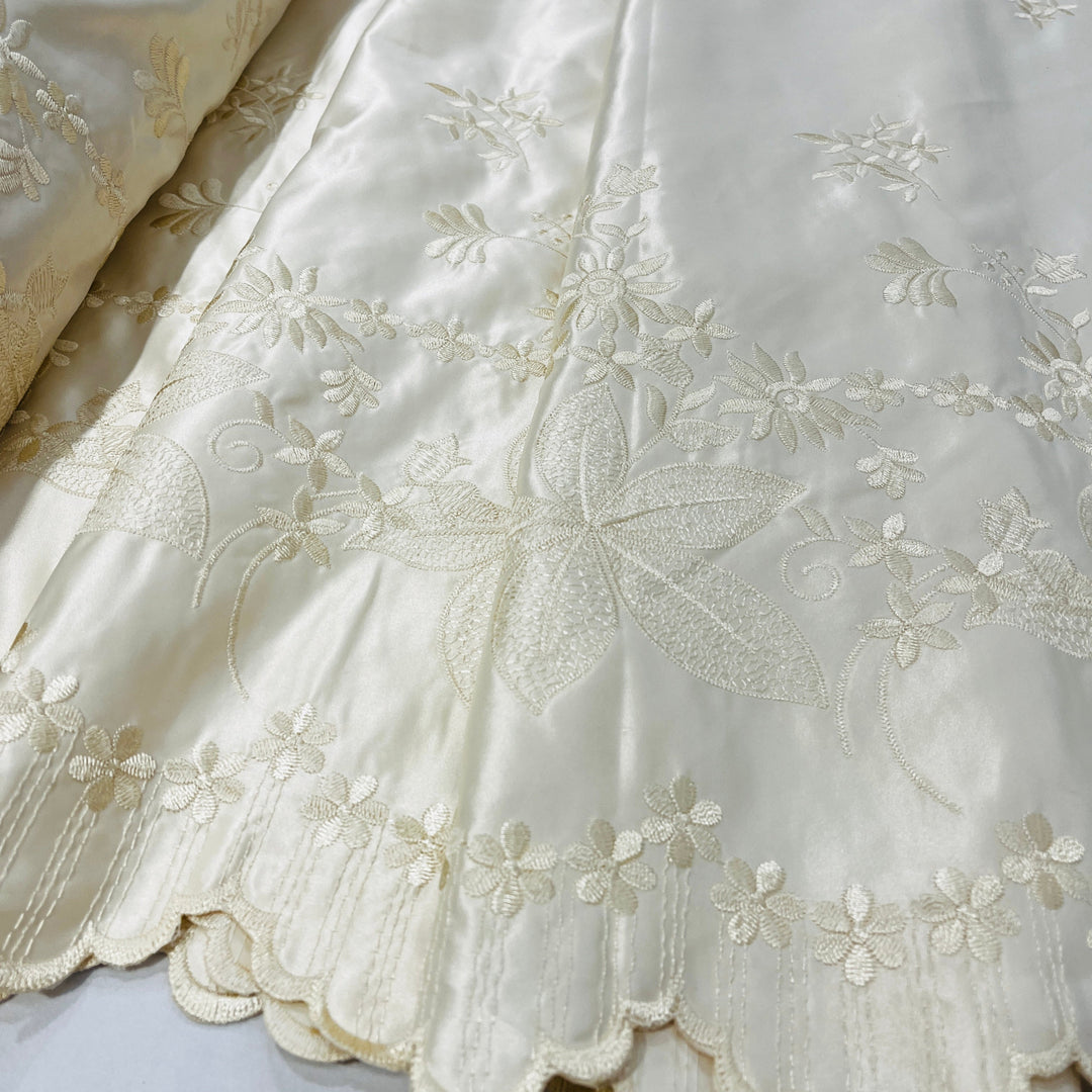 Close-up of an champagne satin fabric with delicate floral embroidery and a scalloped embroidered border.